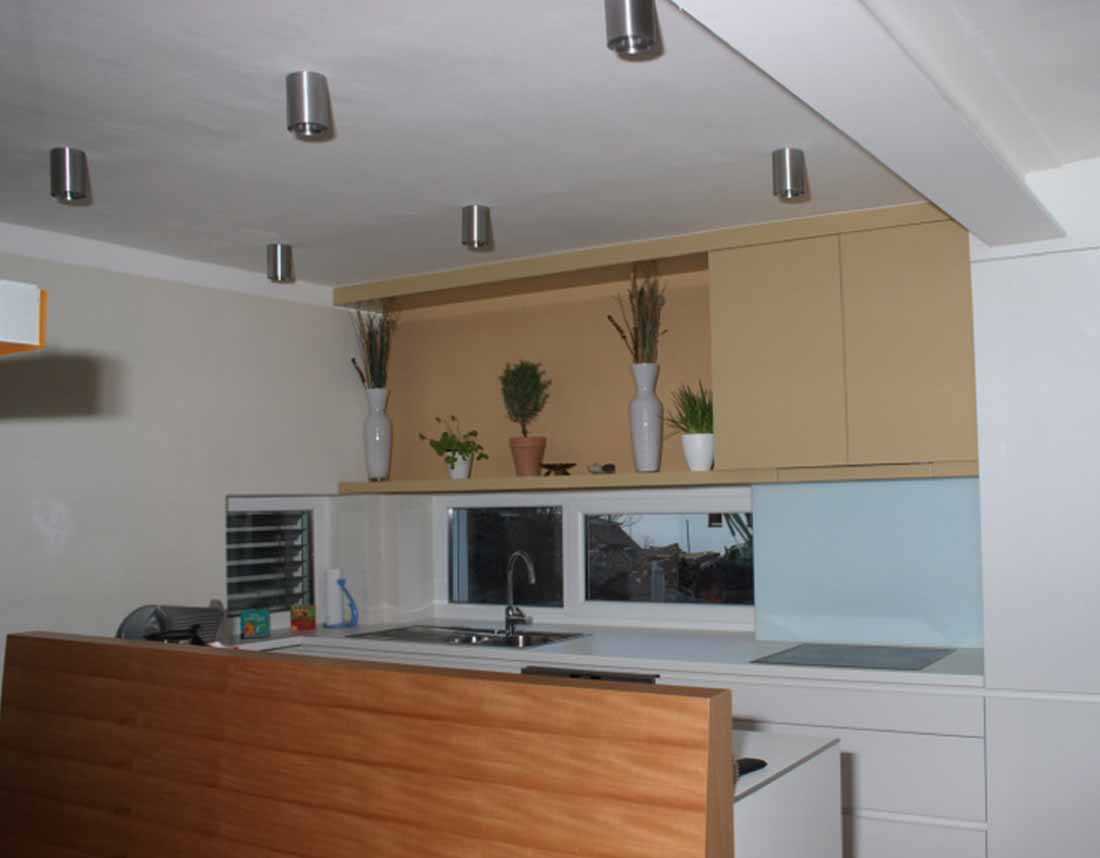 Moderne grifflose Hochglanzküche in Weiß mit minimalistischen Schränken, Dekorationspflanzen und Deckenspots.