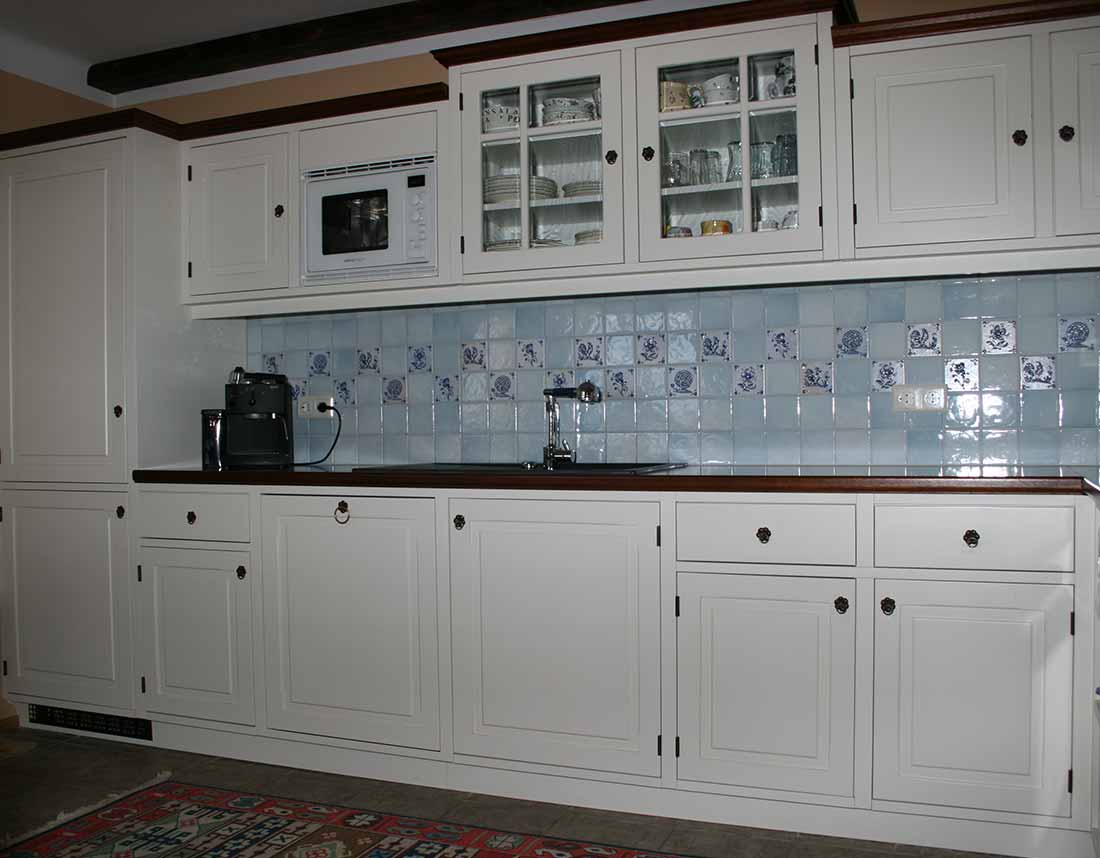 Weiße Massivholzküche im Rahmenbau mit Fliesenrückwand und integrierter Mikrowelle, Glasvitrine und Kaffeemaschine.