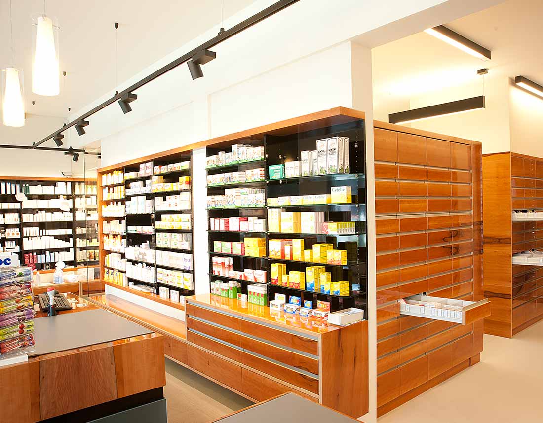 Medikamente in einem modernen Regal mit Holz- und Glaselementen in einer Apotheke.