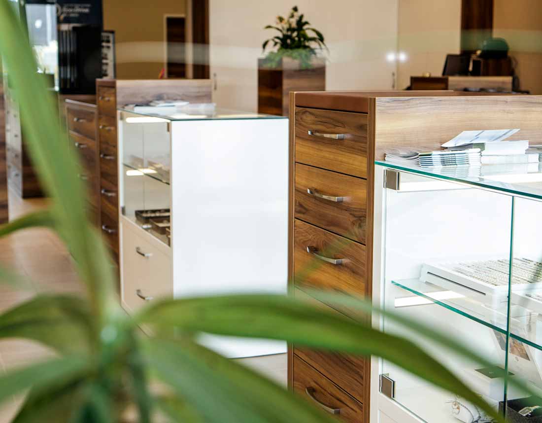 Holzkommoden und beleuchtete Glasvitrinen in einem modernen Raum, mit Pflanzen im Vordergrund.