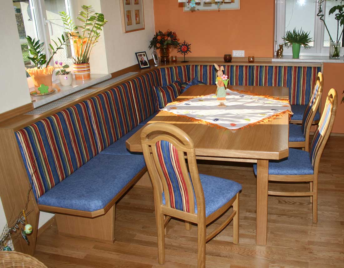 Essbereich mit Holztisch, Eckbank und Stühlen, dekoriert mit gestreiften Polstern und Osterdekoration.