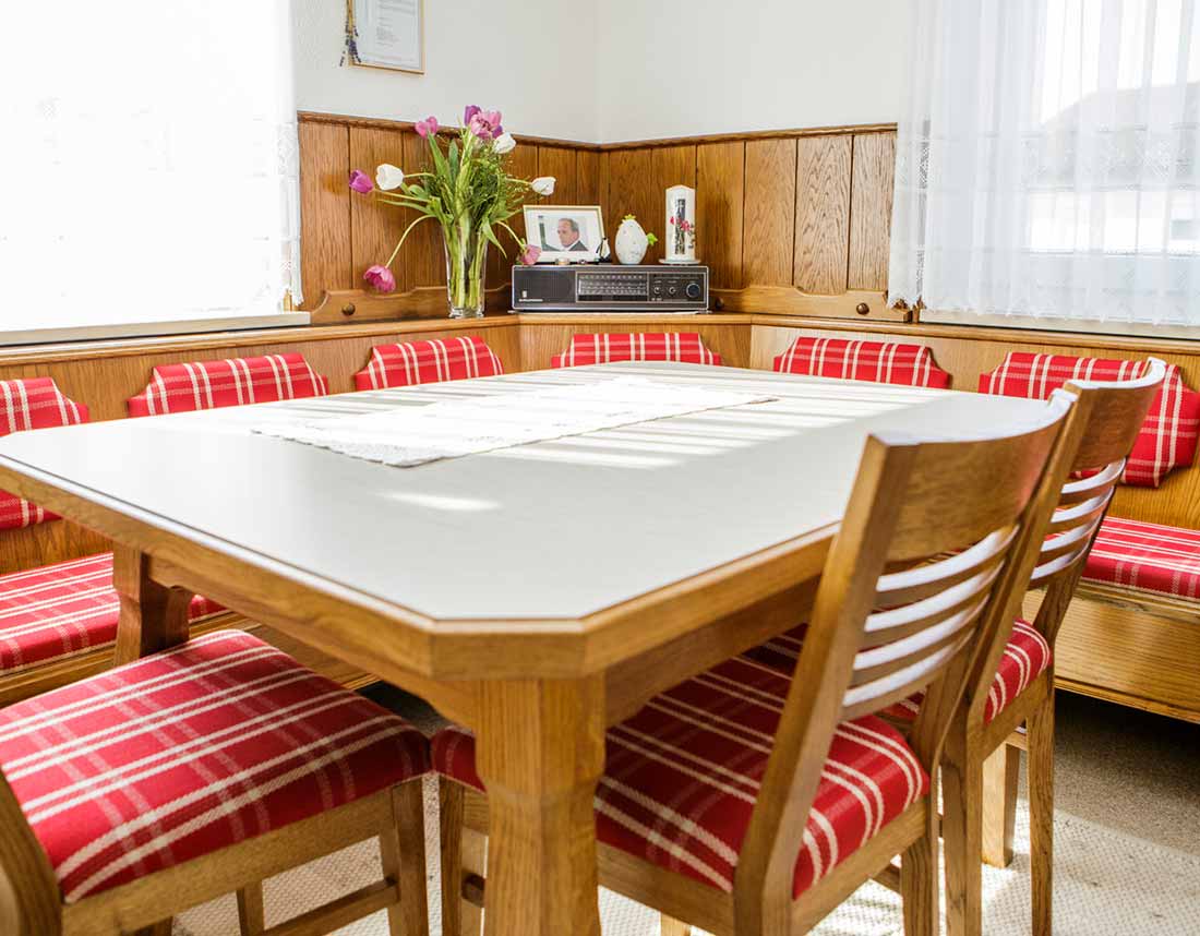 Essbereich mit Holztisch, roten, karierten Stühlen und Bankpolstern.