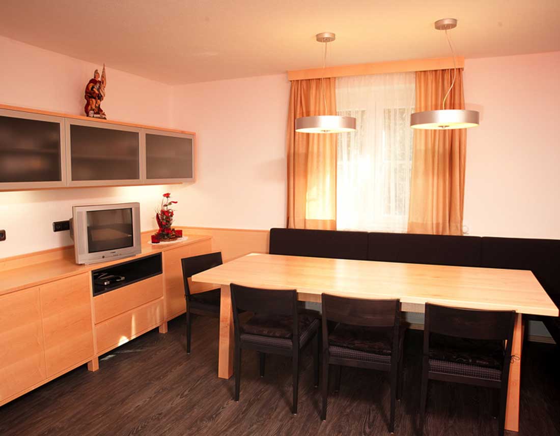 Esszimmer mit hellem Holztisch, schwarzen Stühlen und integriertem TV-Bereich