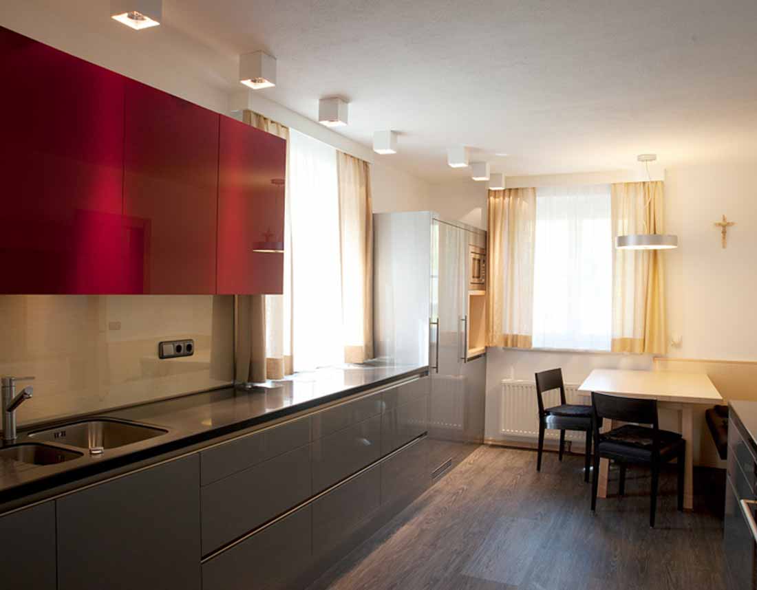 Moderne Küche mit glänzenden roten Oberschränken und grauen Unterschränken in saniertem Altbau.