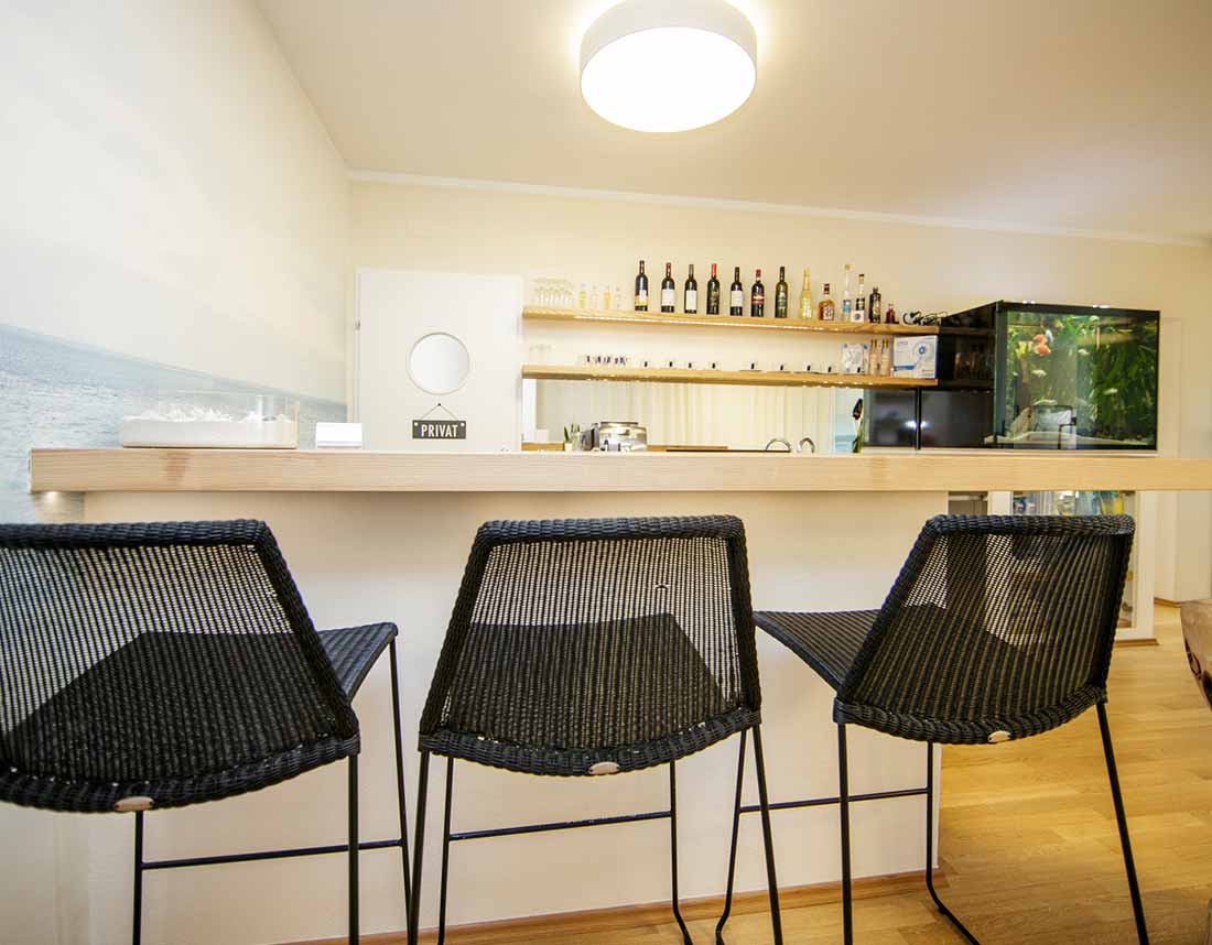 Moderne Bar aus hellem Holz mit schwarzem Hocker-Set und dekorativer Rückwand.
