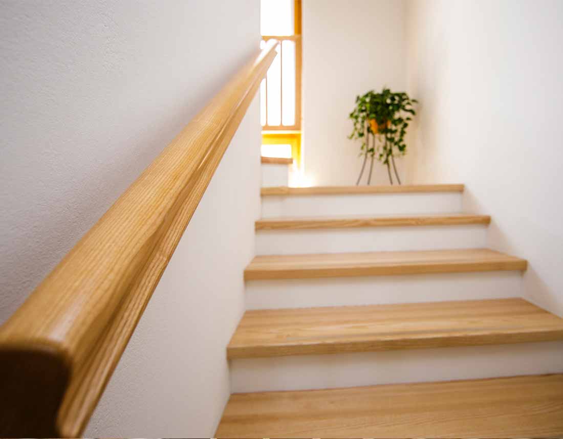 Holztreppe mit schlichtem Geländer und Pflanze im Hintergrund.