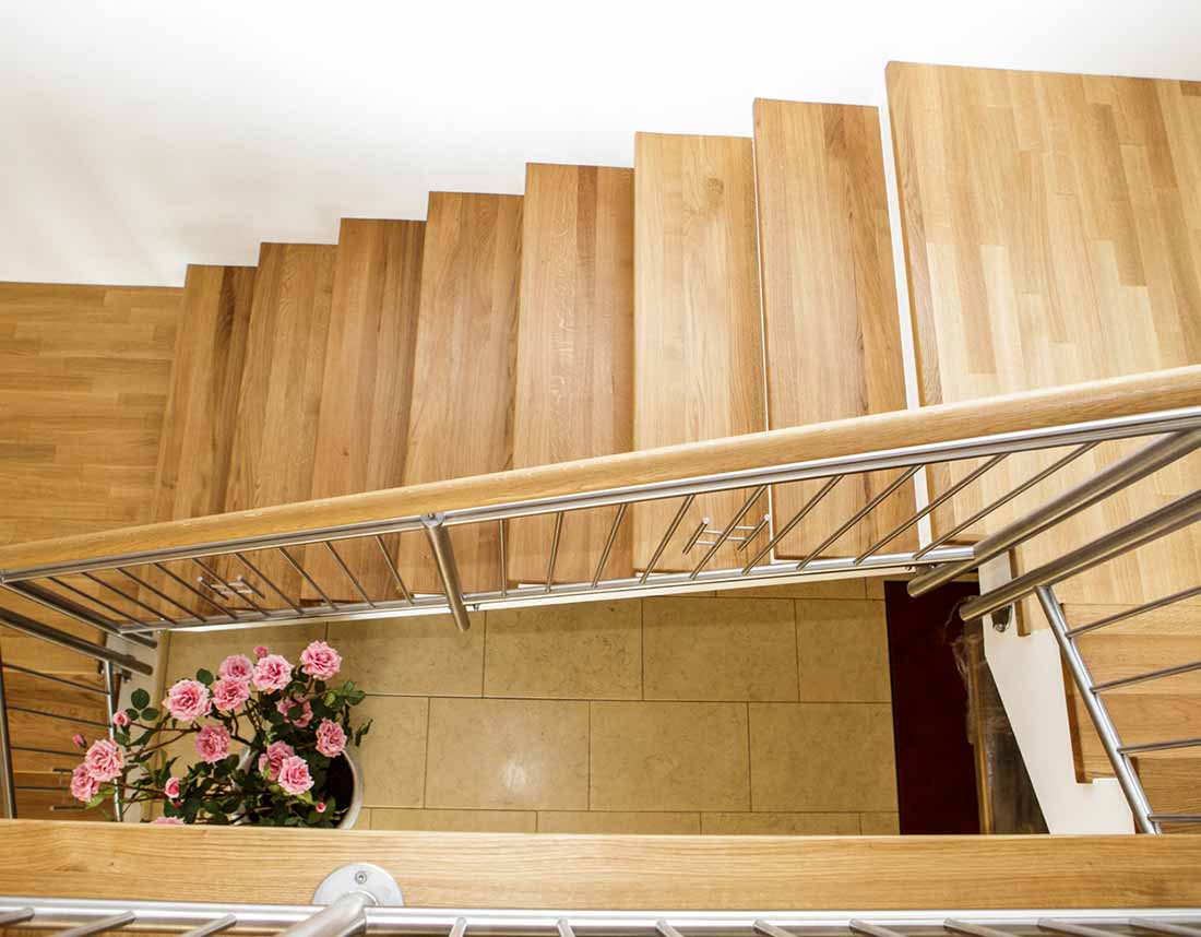 Blick von oben auf eine Holztreppe mit Pflanzenarrangement im Erdgeschoss.