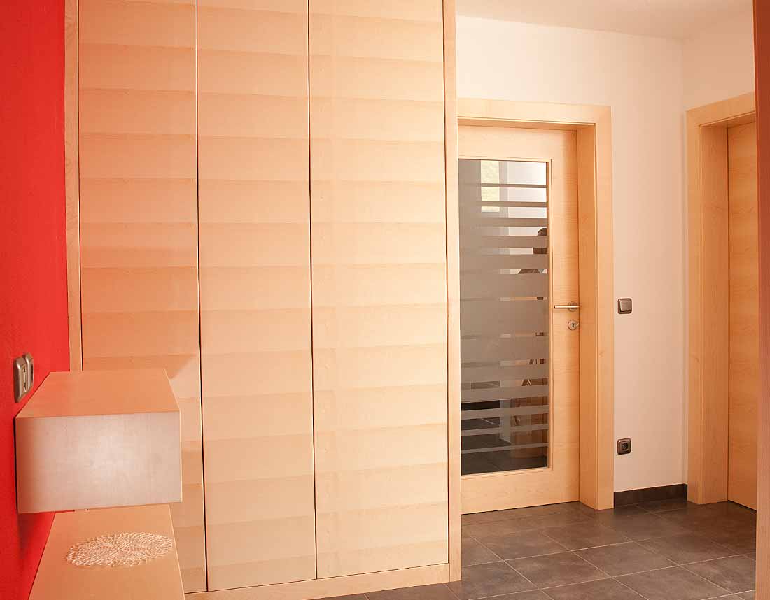 Ein heller Eingangsbereich mit modernen Holzschränken und roten Wänden.
