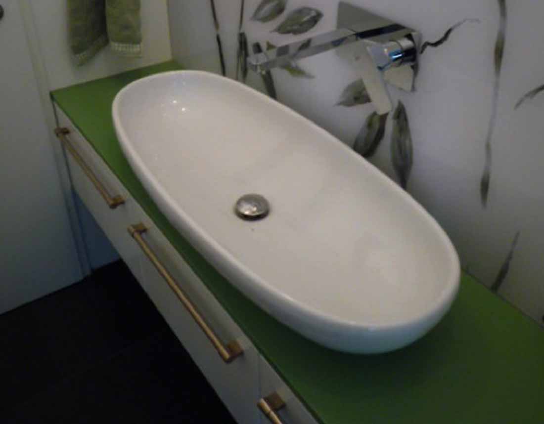 Ein ovale Waschschüssel mit grüner Arbeitsplatte und Wandleuchte im Hintergrund.