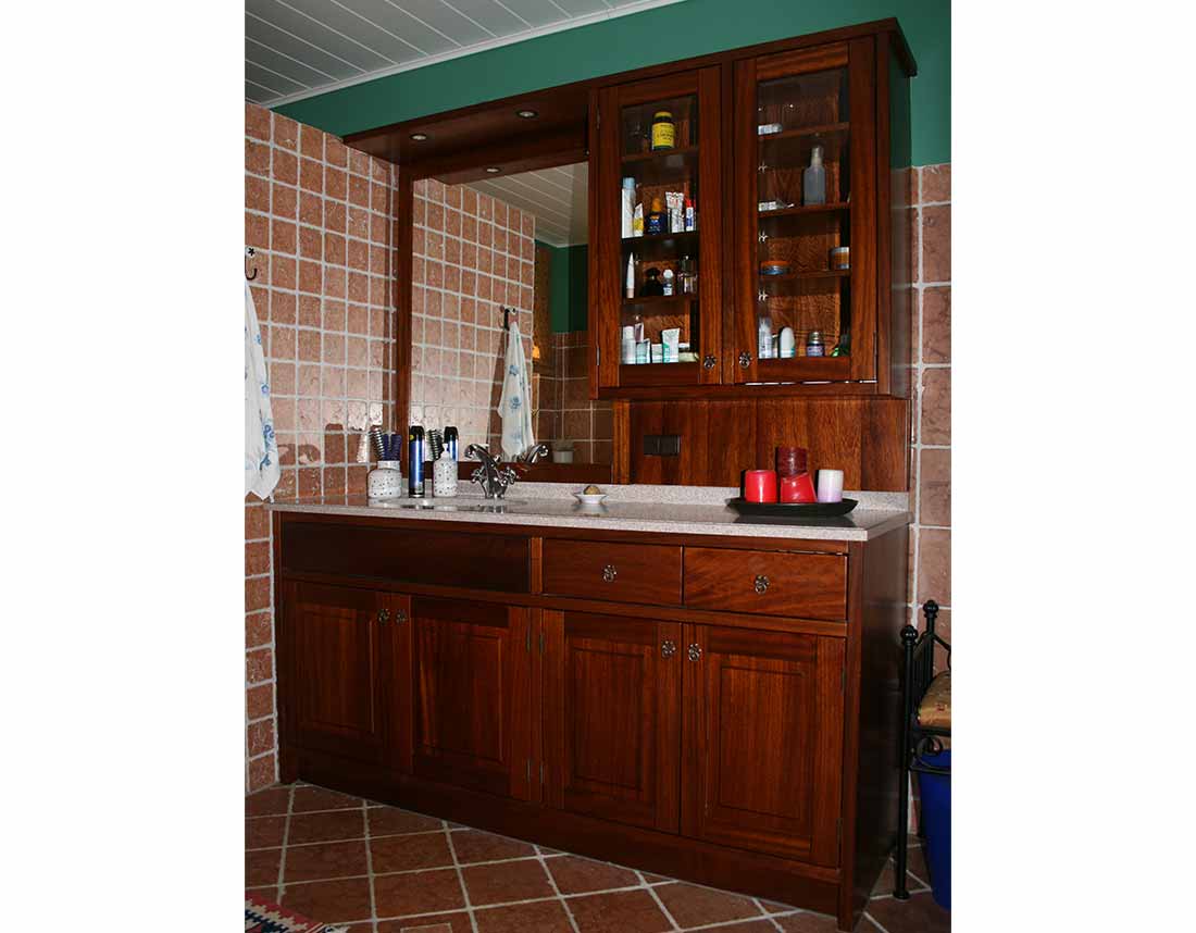 Badezimmer-Waschtischverbau aus dunklem Massivholz mit Glasfront und Fliesenwand.