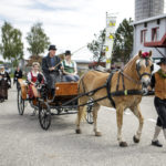 Eine Pferdekutsche mit einem Fahrer und zwei Frauen in Tracht wird von einem Pferd gezogen.