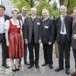 Sechs Personen, darunter Männer in Trachten und eine Frau im Dirndl, posieren für ein Gruppenfoto.