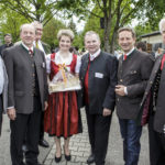 Sechs Männer und eine Frau in Tracht posieren lächelnd, die Frau hält einen Geschenkkorb.