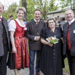Vier Männer und eine Frau in Tracht posieren für ein Foto bei einem Jubiläumsfest im Freien.