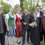 Eine Gruppe von sieben Personen, darunter Männer und Frauen in traditioneller Tracht, posiert lächelnd für ein Foto.