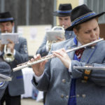 Eine Blaskapelle spielt im Freien, Musiker in blauen Uniformen, eine Frau spielt Querflöte.