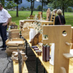 Mehrere handgefertigte Holzobjekte werden auf einem Tisch im Freien während eines Jubiläumsfestes ausgestellt.