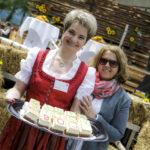 Eine Frau in traditioneller Tracht hält ein Tablett mit Kuchen, auf dem „90 Jahre Erschen“ steht.