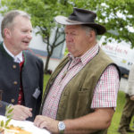 Zwei Männer, einer in traditioneller Tracht, der andere im Cowboy-Hut, unterhalten sich bei einer Feier.