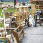 Ein Flohmarktstand mit Holzstühlen, Vogelhäuschen und Töpfen, auf einer Straße aufgebaut.