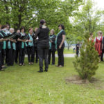 Ein Chor singt draußen bei einer Veranstaltung, während Zuschauer in traditioneller Kleidung zusehen.