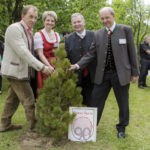 Vier Personen pflanzen gemeinsam einen Baum, daneben steht ein Schild mit dem Erschen-Logo.