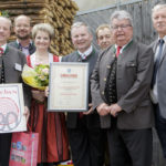 Sechs Personen posieren mit einer Urkunde und dem Erschen-Logo, eine Frau hält einen Blumenstrauß.