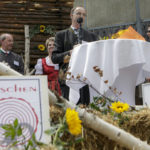 Ein Mann spricht am Mikrofon, im Vordergrund das Erschen-Logo, Strohballen und Sonnenblumen.