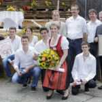 Eine Gruppe von Personen, einige halten Auszeichnungen und Urkunden, posiert vor einer festlich dekorierten Bühne.