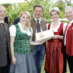 Fünf Personen in traditioneller Kleidung, eine Frau hält ein Geschenk mit dem Wappen des Kärntner Landtags.