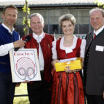 Vier Personen, darunter eine Frau in Tracht, posieren mit einem Geschenk und einem Schild mit dem Erschen-Logo.