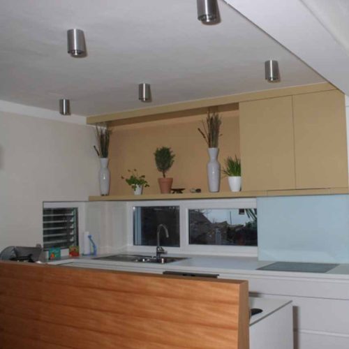 Moderne grifflose Hochglanzküche in Weiß mit minimalistischen Schränken, Dekorationspflanzen und Deckenspots.