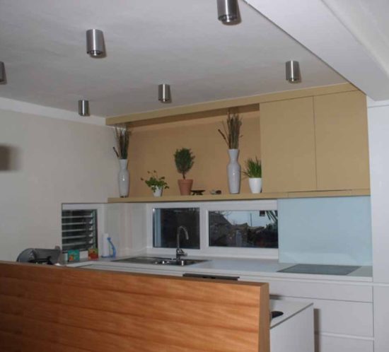 Moderne grifflose Hochglanzküche in Weiß mit minimalistischen Schränken, Dekorationspflanzen und Deckenspots.