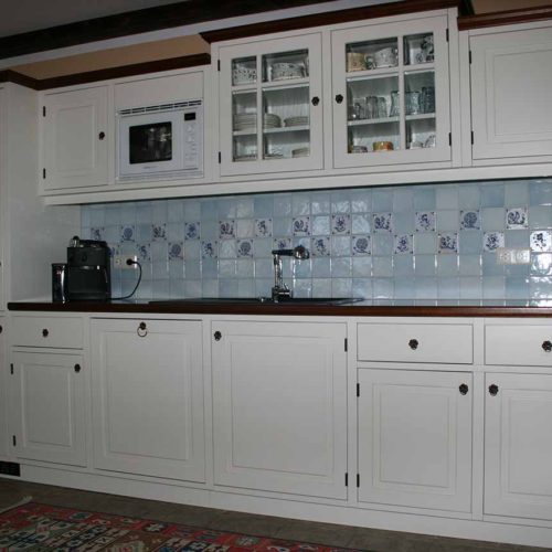 Weiße Massivholzküche im Rahmenbau mit Fliesenrückwand und integrierter Mikrowelle, Glasvitrine und Kaffeemaschine.