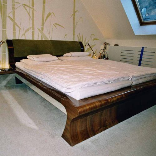 Doppelbett aus dunklem Walnussholz mit grüner Rückenlehne.