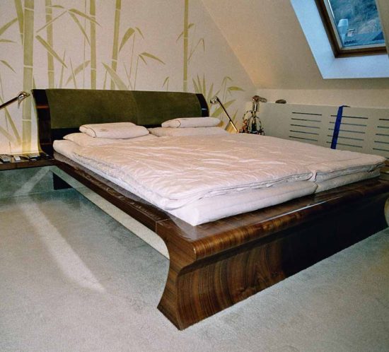 Doppelbett aus dunklem Walnussholz mit grüner Rückenlehne.