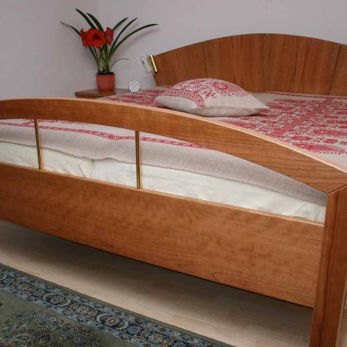 Doppelbett aus Kirschholz mit gebogenem Kopf- und Fußteil, elegant dekoriert.