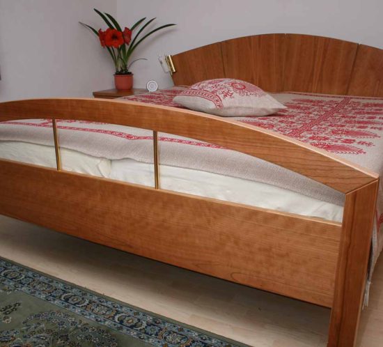 Doppelbett aus Kirschholz mit gebogenem Kopf- und Fußteil, elegant dekoriert.