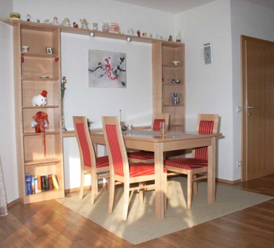 Essbereich mit hellen Holzmöbeln, rot gestreiften Polsterstühlen und Regalen voller Dekorationsgegenstände.