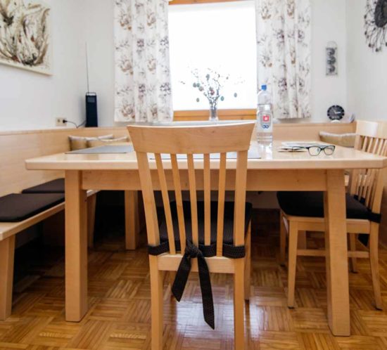 Heller Essbereich mit Holztisch, Stühlen und gepolsterter Eckbank vor einem Fenster.