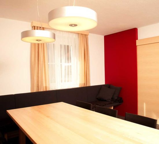 Essbereich mit hellem Holztisch, schwarzer Eckbank und zwei modernen Deckenleuchten.