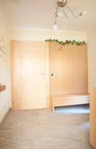 Helle Holztür neben einer passenden Garderobe mit Sitzbank und Hakenleiste, dekoriert mit grünen Pflanzen.