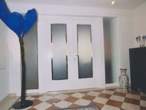 Doppelflügeltür mit Milchglasscheiben, daneben eine blaue Skulptur und dekorative Vase.