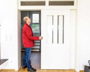 Mann in roter Jacke öffnet weiße Schiebetür mit Glaseinsätzen.