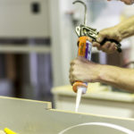 Handwerker verwendet eine Kartuschenpistole zum Auftragen von Klebstoff auf ein Holzstück.