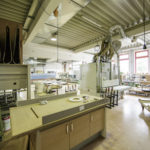 Werkstattbereich mit Holzbearbeitungsmaschinen und Werkbänken, umgeben von Werkzeugen und Materialien.