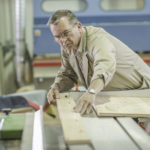 Ein Handwerker richtet ein Holzbrett auf einer Säge in einer Werkstatt sorgfältig aus.