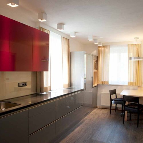 Moderne Küche mit glänzenden roten Oberschränken und grauen Unterschränken in saniertem Altbau.