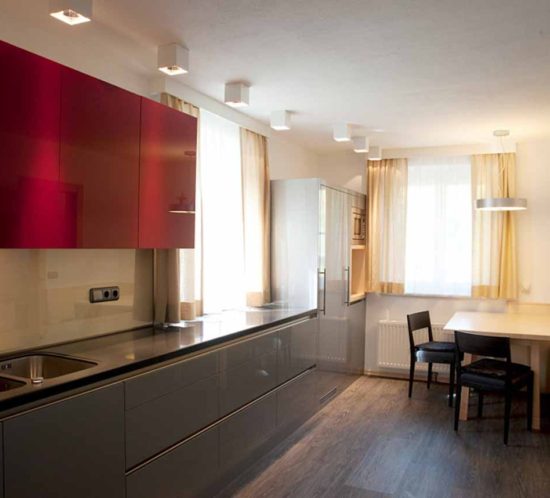 Moderne Küche mit glänzenden roten Oberschränken und grauen Unterschränken in saniertem Altbau.