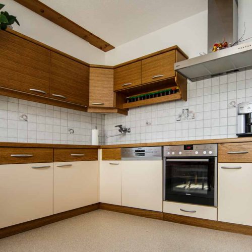 Küche mit Holz- und Creme-Fronten, Backofen, Dunstabzugshaube, Geschirrspüler und Gewürzablagen.